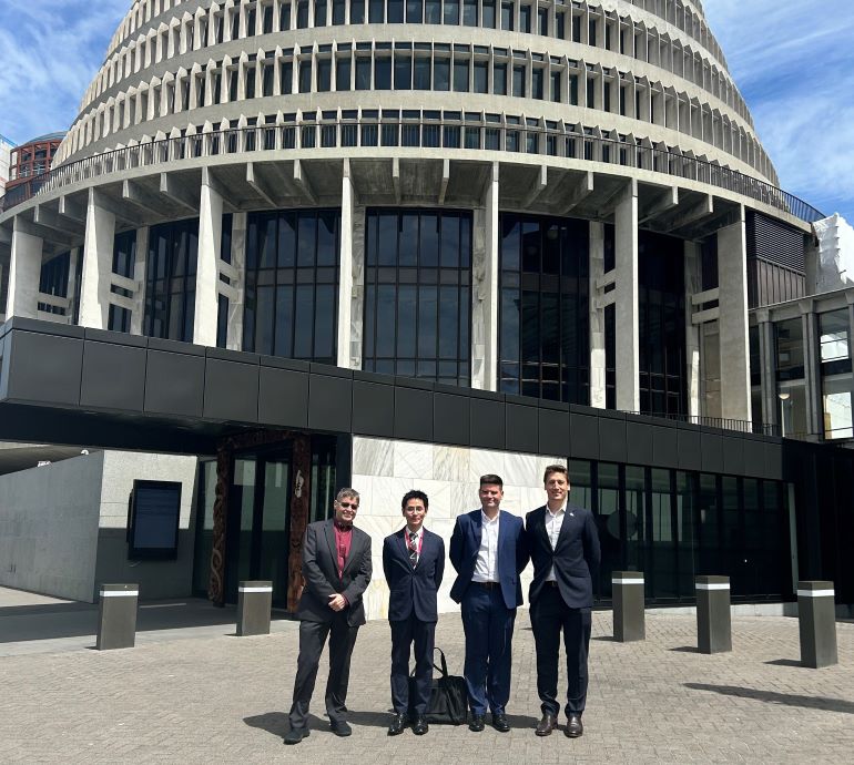 4 men in business suits stand outside the Beehive building